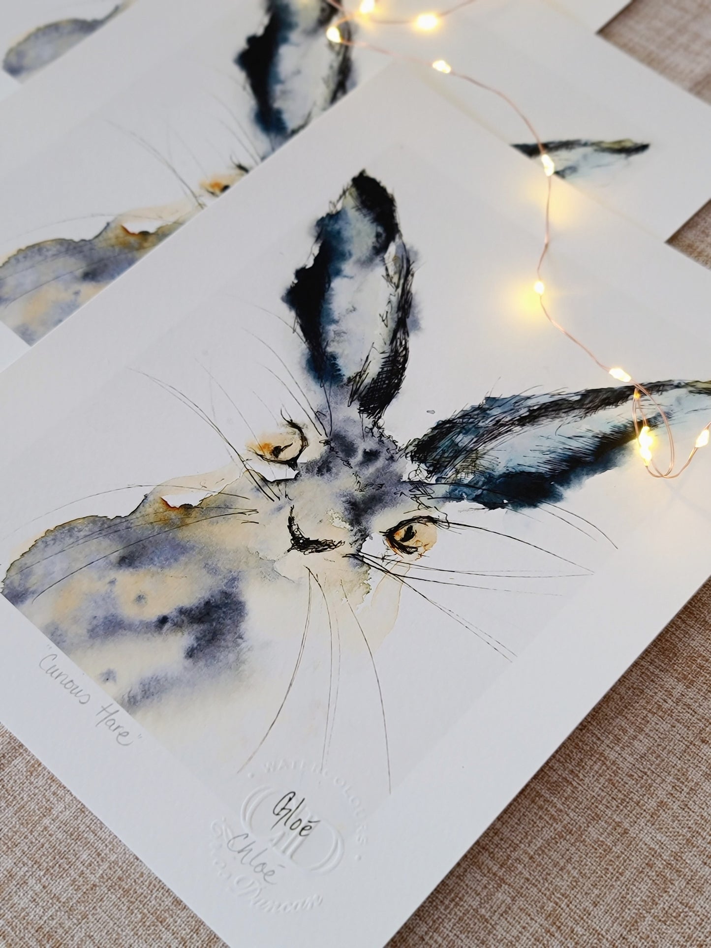 Watercolor painting of a gentle hare with upright ears. Surrounded by open white space, the soft brushwork captures a moment of quiet curiosity. Created by Scottish artist Chloe Duncan, whose work blends animals and quiet emotion.